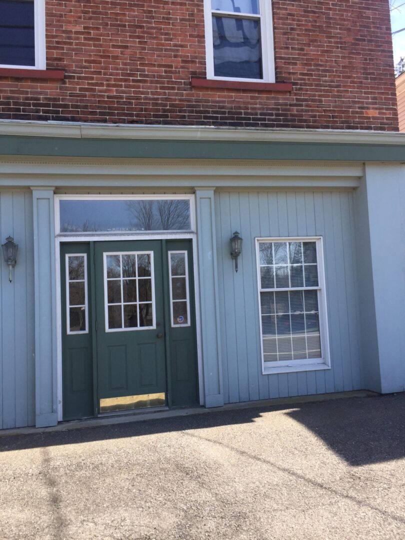 A green door and two windows in front of a building.