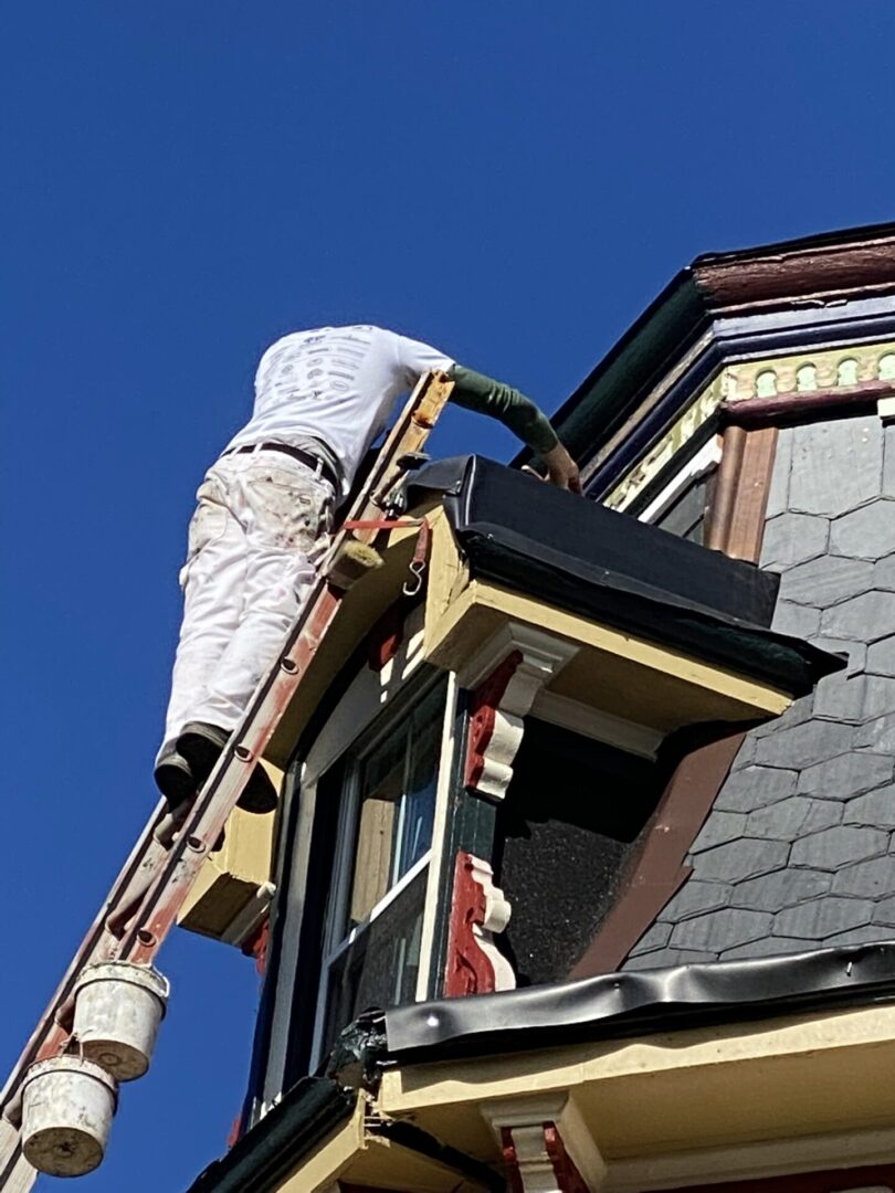 A man on a ladder painting the side of a building.